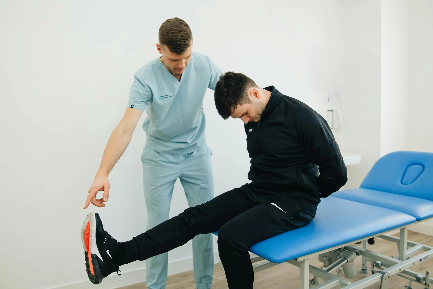 Körpermanufaktur - Physiotherapie. Osteopathie. Naturheilkunde – Dieses Bild scheint einen Physiotherapeuten zu zeigen, der eine Untersuchung des Bewegungsapparates an einem Patienten durchführt, der auf einer Behandlungsliege sitzt.
